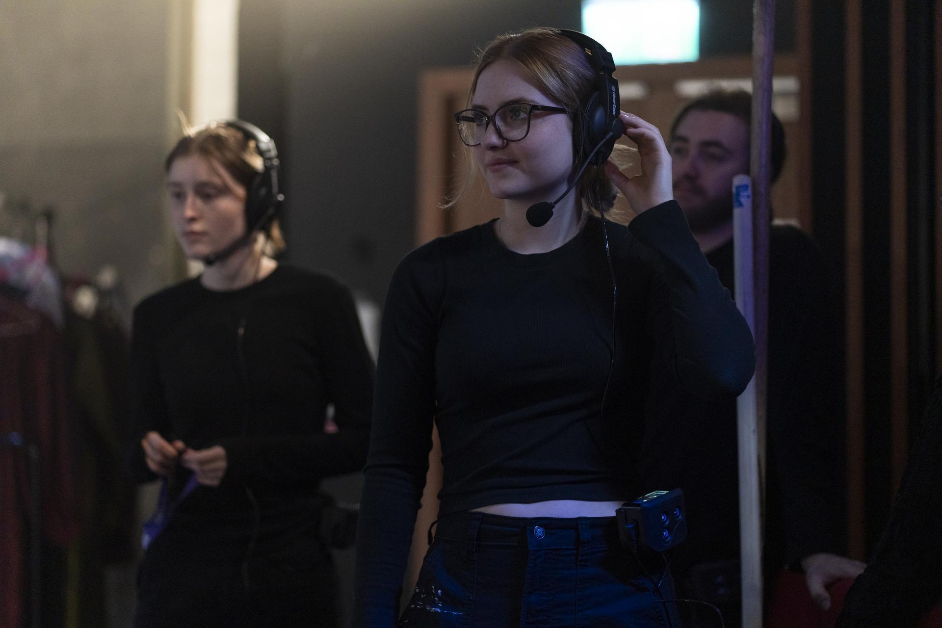 Backstage crew member wearing a headset and microphone adjusts her earpiece while working behind the scenes